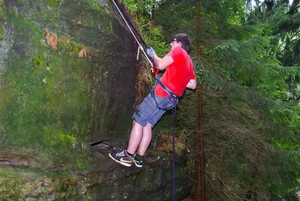 Kletterer sichert sich mit Seil an einer steilen Felswand im Wald