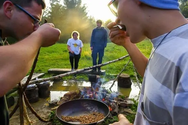Kochen von Insekten über offenem Feuer in einer Pfanne, zwei Personen essen