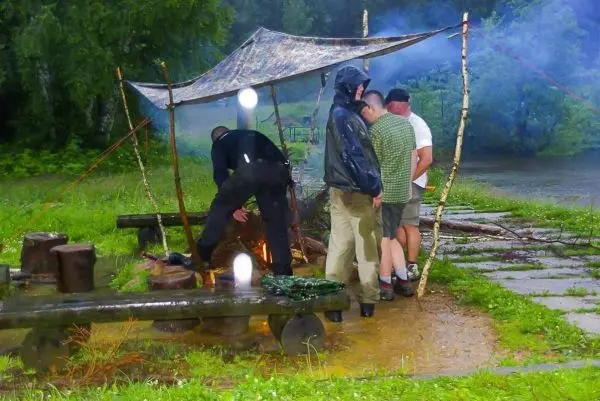 Männer stehen unter einem Tarp und bereiten ein kleines Bodenfeuer vor
