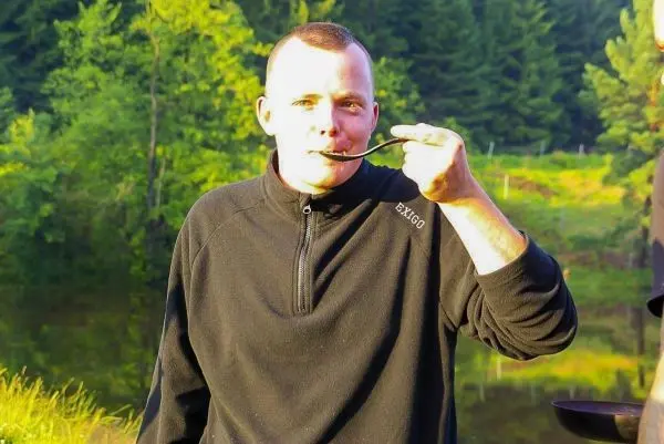 Mann hält einen Löffel an den Mund und probiert Essen