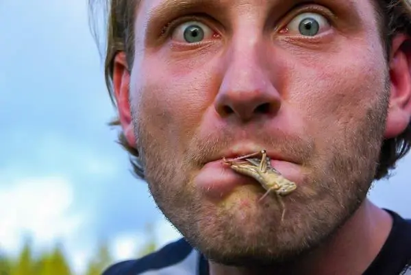 Mann mit Heuschrecke im Mund und überraschter Mimik