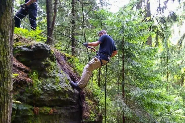 Mann seilt an einem Felsen mit Seil und Karabiner im Wald ab