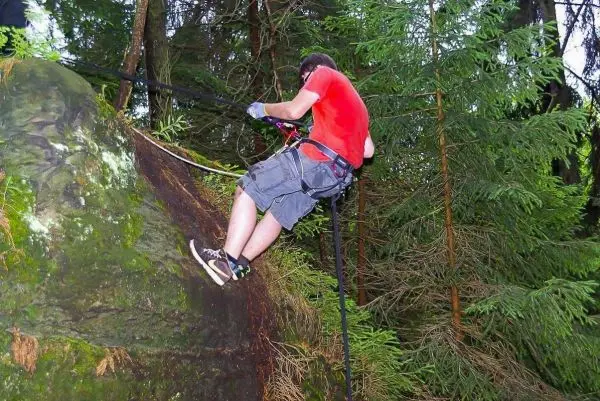 Person seilt an einem Felsen mit Sicherungsseil und Kletterausrüstung ab