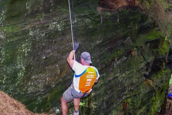 Person seilt an einem Felsvorsprung ab, gesichert mit einem Seil