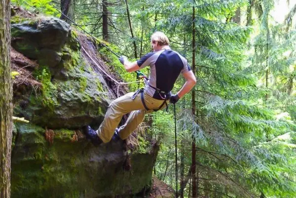 Person seilt an einer Felswand im Wald ab