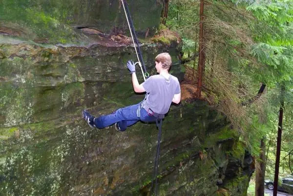 Person seilt an einer Felswand mit Sicherungsseil und Kletterausrüstung