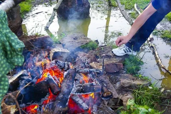 Person sitzt neben einem Feuer und legt Holz nach