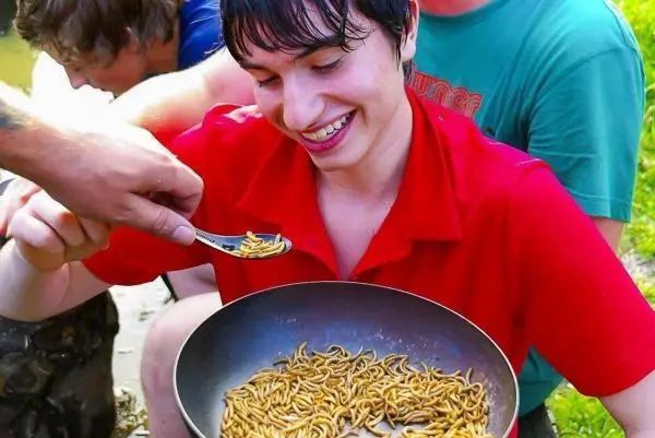 Schüssel mit essbaren Insekten vor lächelndem Teilnehmer, der mit Löffel entnimmt