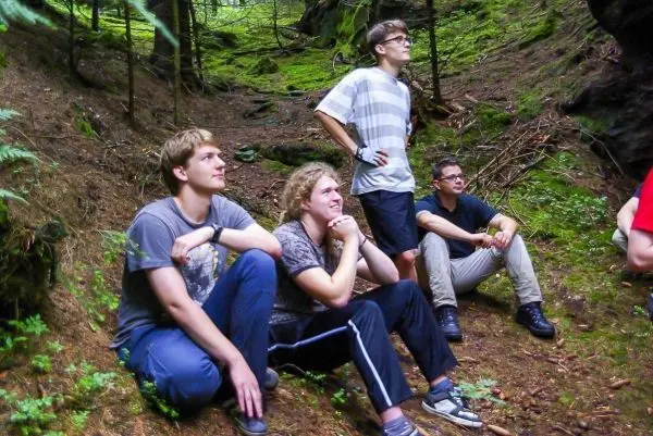 Vier Personen sitzen im Wald auf dem Boden und schauen nach oben