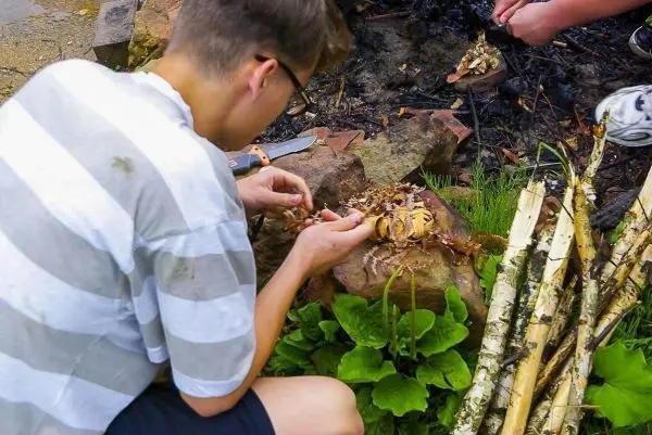Zunder wird auf einem Stein vorbereitet, während Holzstücke daneben liegen