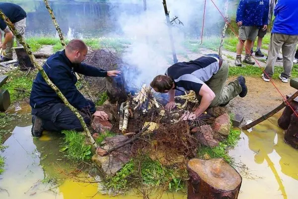 Zwei Personen bauen ein Feuer aus Ästen und Holz