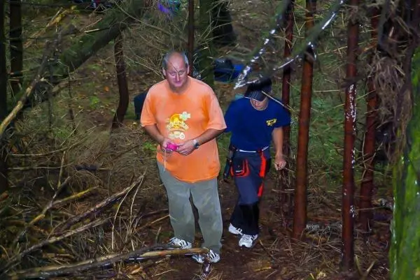 Zwei Personen bewegen sich durch einen bewaldeten Bereich mit umgestürzten Ästen