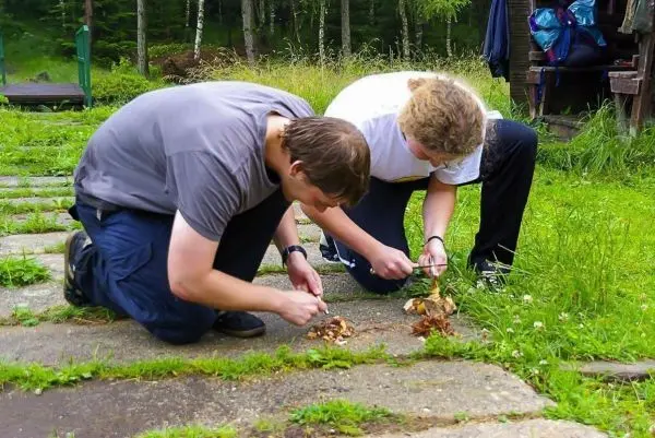Zwei Personen knien auf dem Boden und bearbeiten Zunder mit einem Messer