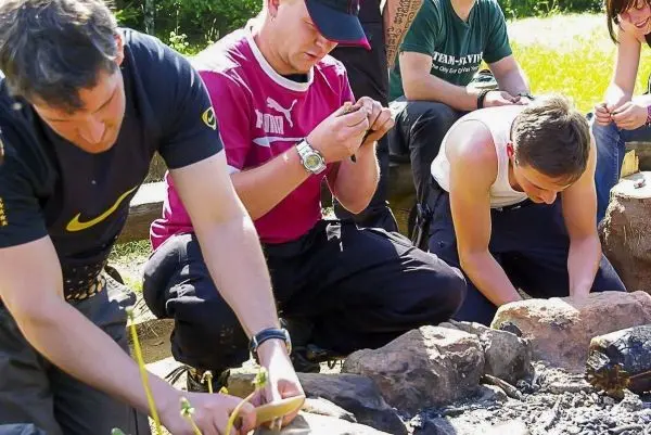 Drei Personen bearbeiten Zunder in der Nähe eines kleinen Lagerfeuers