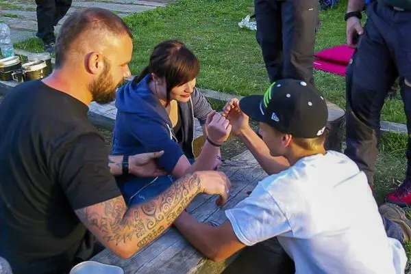 Drei Personen sitzen an einem Tisch und führen ein Armdrücken durch