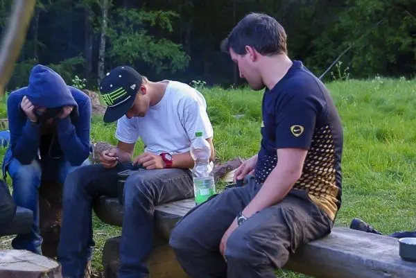 Drei Personen sitzen auf einer Holzbank und beschäftigen sich mit verschiedenen Aktivitäten