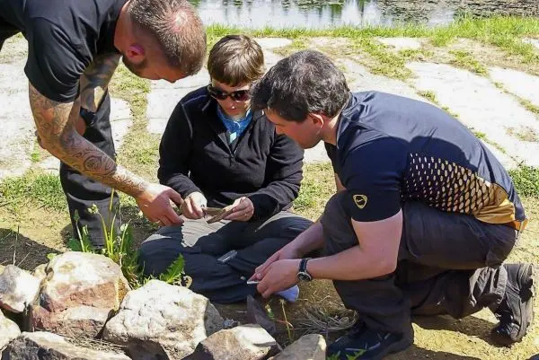 Drei Personen sitzen um einen Steinhaufen und bearbeiten ein Werkzeug