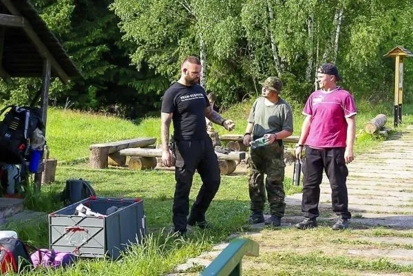 Drei Personen stehen auf einer Wiese neben Ausrüstung und Rucksäcken