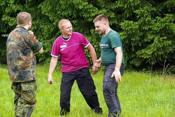 Drei Personen stehen auf einer Wiese und interagieren miteinander