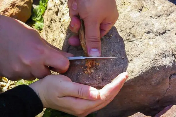Ein Messer schneidet Holz auf einem Stein, während eine Hand das Stück hält