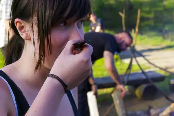 Frau trinkt aus einer Tasse, im Hintergrund wird ein Feuer vorbereitet