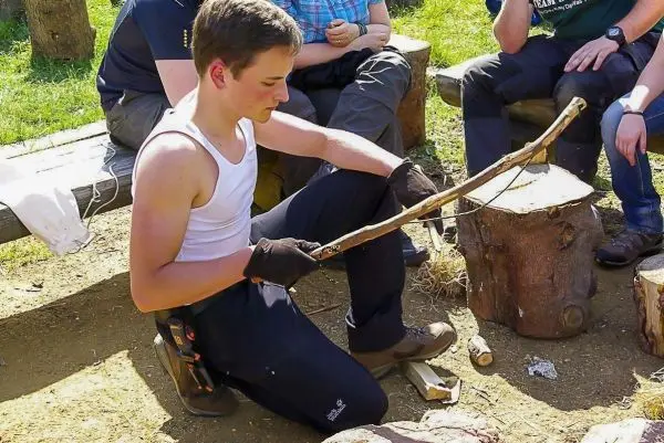 Junger Mann bearbeitet einen Stock mit einem Messer auf einem Holzblock