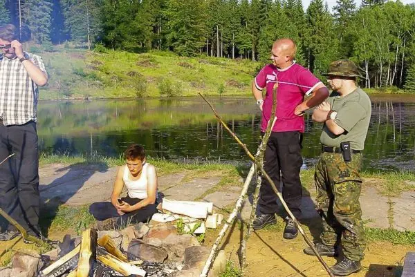 Kleines Bodenfeuer brennt vor mehreren Personen am Ufer eines Gewässers