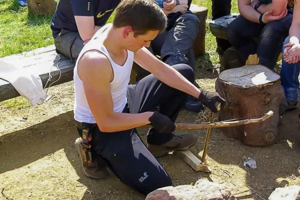 Mann bearbeitet Holzstück mit einem Messer auf dem Boden
