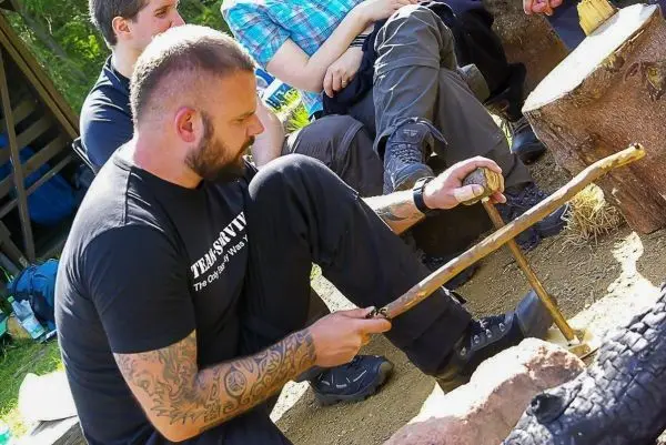 Mann bearbeitet Holzstück mit einem Messer auf einem Baumstamm