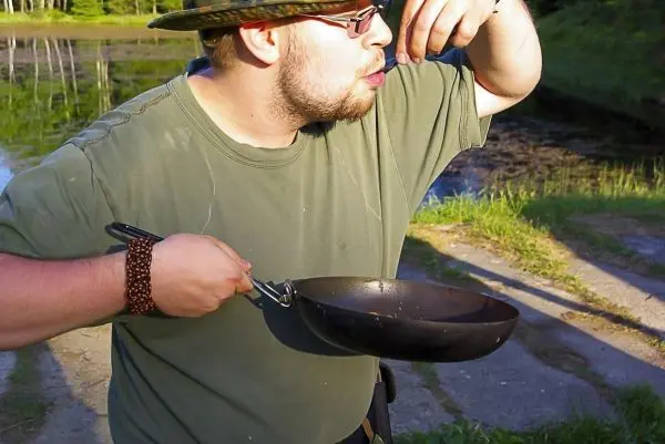 Mann hält Pfanne und löffelt Inhalt mit einer Gabel