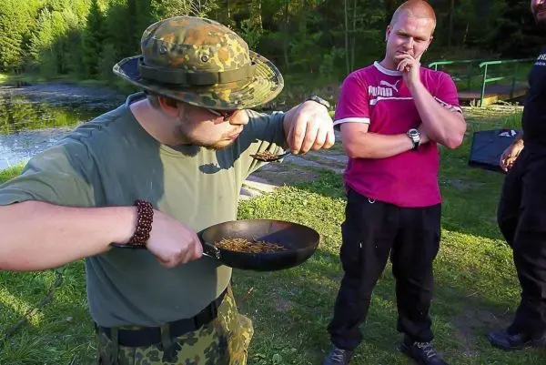 Mann mit Feldmütze hält Pfanne mit Insekten und betrachtet sie aufmerksam