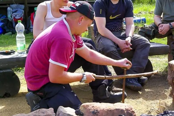 Mann nutzt einen Feuerbohrer zur Zunderentzündung am Lagerfeuer