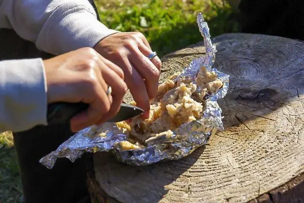 Messer schneidet in Alufolie eingewickeltes Essen auf einem Baumstumpf