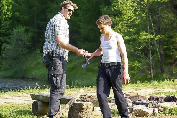 Messer wird von einer Person an eine andere übergeben, im Hintergrund ein Lagerfeuer