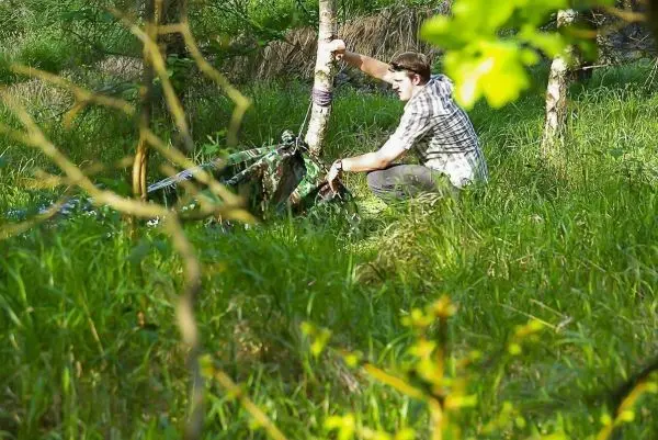 Person befestigt Seil an Baum im Gras
