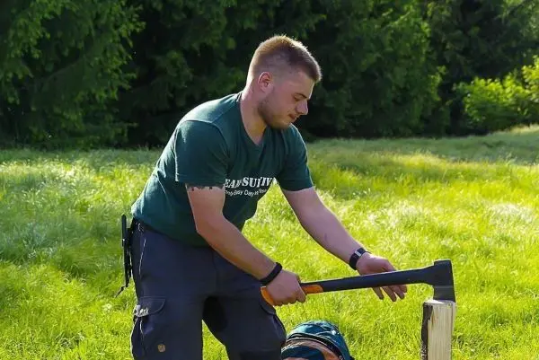 Person hackt mit einer Axt auf einen Holzblock beim Überlebenstraining