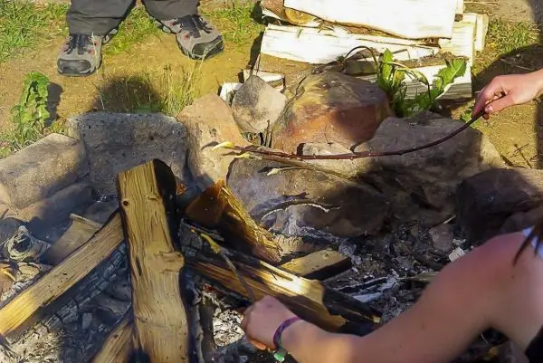 Person hält Stock über Feuerstelle beim Kochen im Outdoorkurs