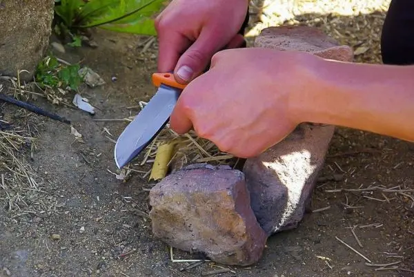 Person schneidet mit einem Messer Holzstück auf dem Boden
