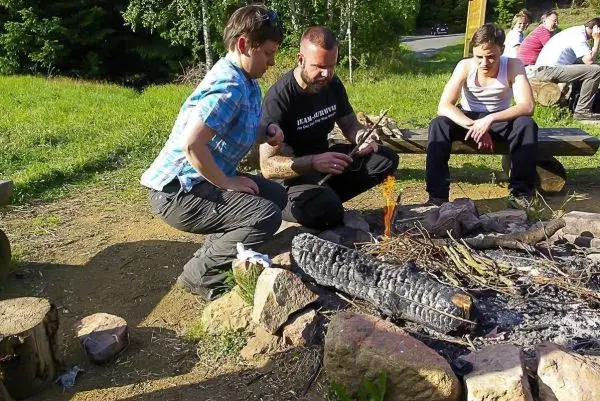 Person zündet Feuerstelle an, während andere zuschauen beim Survival Training