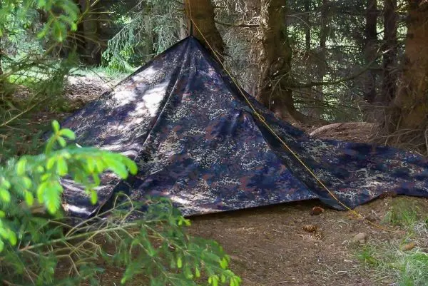 Tarp-Notunterkunft aus camouflagefarbenem Material zwischen Bäumen auf dem Boden