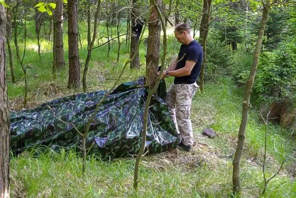 Tarp-Notunterkunft wird zwischen Bäumen aufgestellt und mit Abspannschnur gesichert