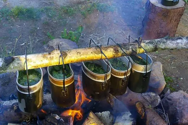 Töpfe hängen an einem Stock über einem Feuer beim Kochen