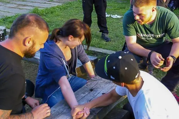 Vier Personen sitzen an einem Tisch und führen ein Armdrücken durch