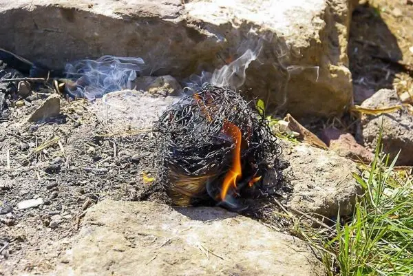 Zunder glimmt und kleine Flamme entsteht auf dem Boden