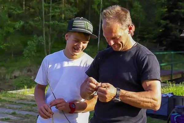 Zwei Personen arbeiten gemeinsam an einem dünnen Stock im Freien