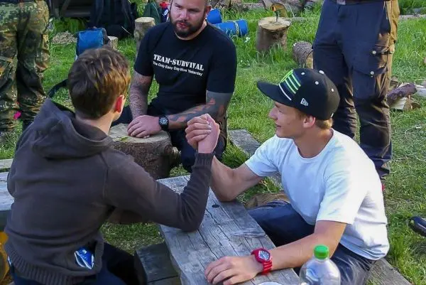 Zwei Personen führen ein Armdrücken an einem Holztisch durch