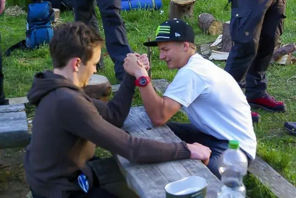 Zwei Personen führen ein Armdrücken an einem Holztisch durch