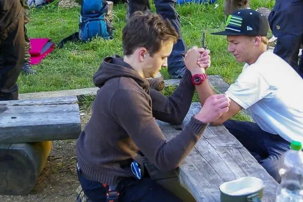 Zwei Personen führen ein Armdrücken an einem Holztisch durch