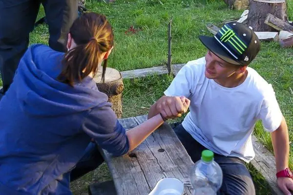 Zwei Personen führen ein Armdrücken auf einem Holztisch durch