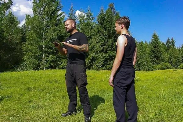 Zwei Personen stehen auf einer Wiese, eine erklärt gestikulierend etwas